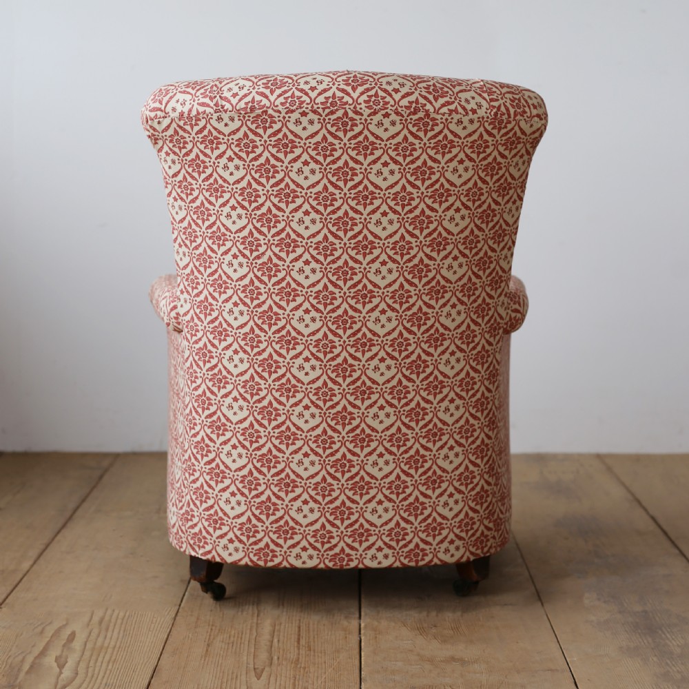 A nineteenth-century Victorian Howard and Sons armchair upholstered in red and cream patterned fabric with a button-backed tufted backrest, deep cushion seat, and turned front legs on brass castors. View IV