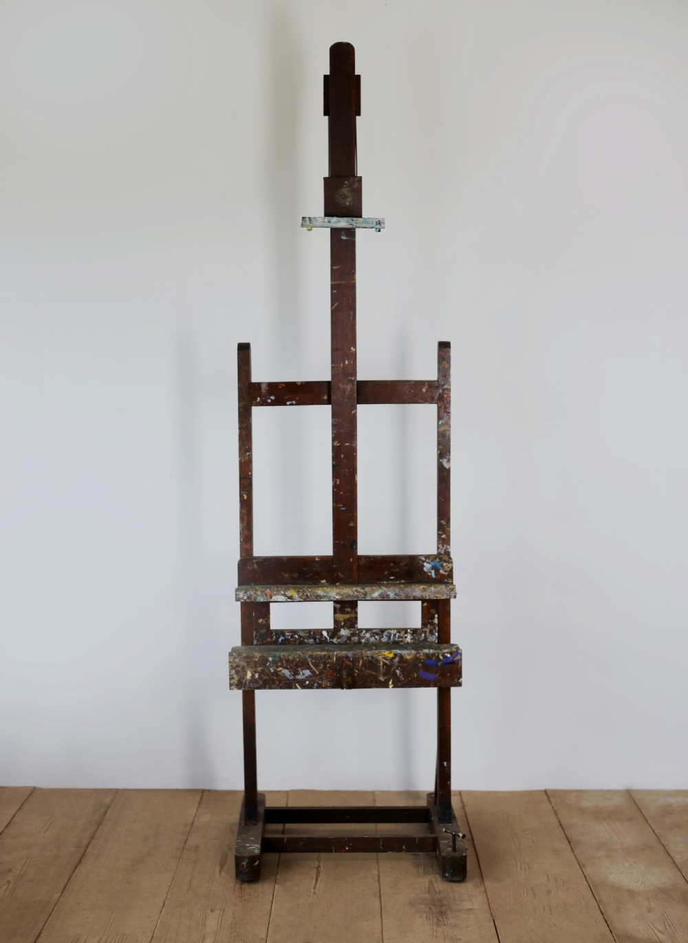 A tall, dark wood nineteenth-century studio easel featuring paint flecks across the adjustable ledge and frame.