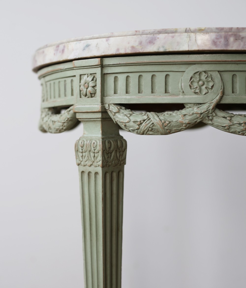 A circular 20th-century gueridon side table with a variegated pink marble top and a sage-green painted wooden frame featuring carved swags and fluted legs. View III
