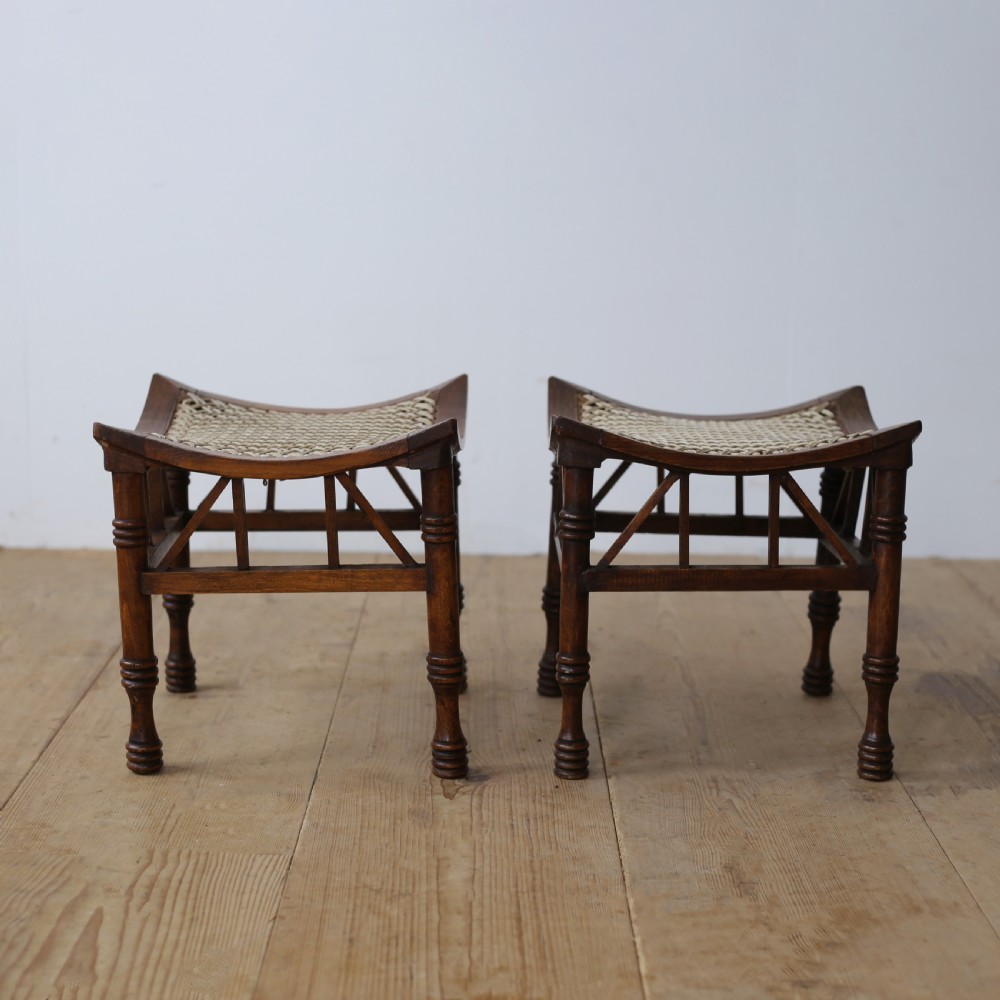 A pair of dark wood stools featuring concave woven cord seats and turned legs with diagonal spindled stretchers.