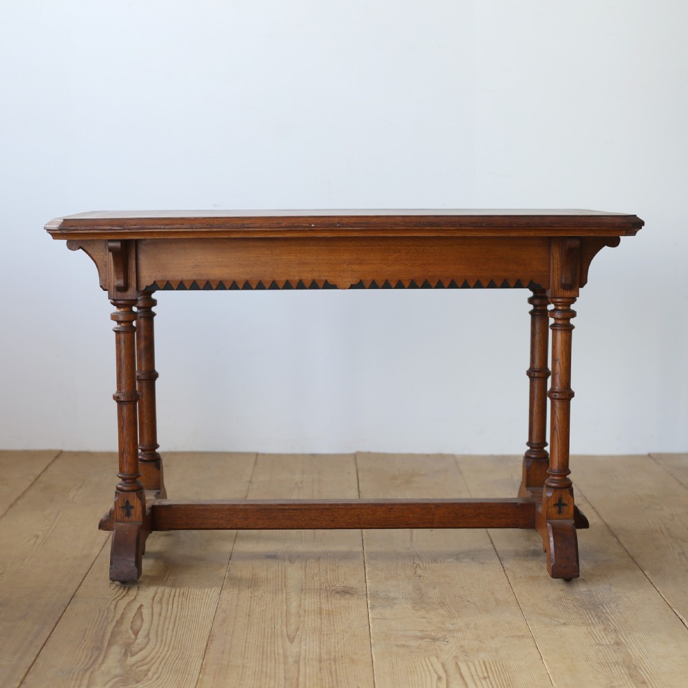 A 19th-century Gothic Revival oak writing table featuring turned columnar legs, a crenellated apron detail, and a low cross-stretcher.