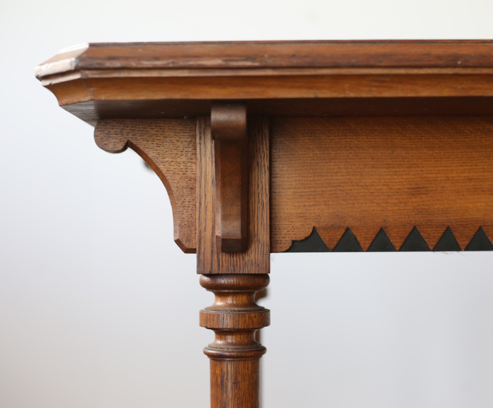 A 19th-century Gothic Revival oak writing table featuring turned columnar legs, a crenellated apron detail, and a low cross-stretcher. View III