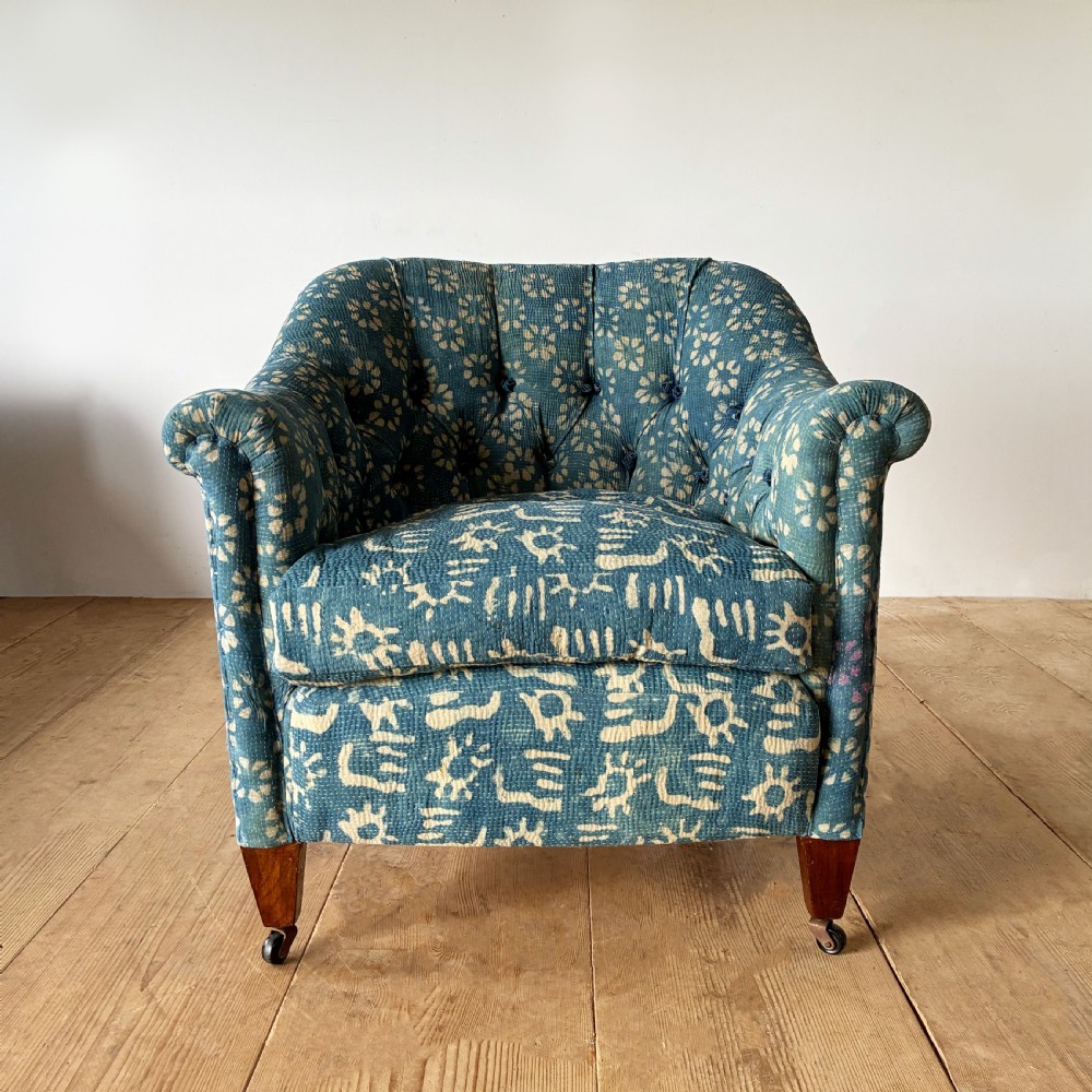 A 19th-century tub chair with blue and cream patterned fabric upholstery, button-tufted backrest, rolled arms, and tapered mahogany legs on brass castors.