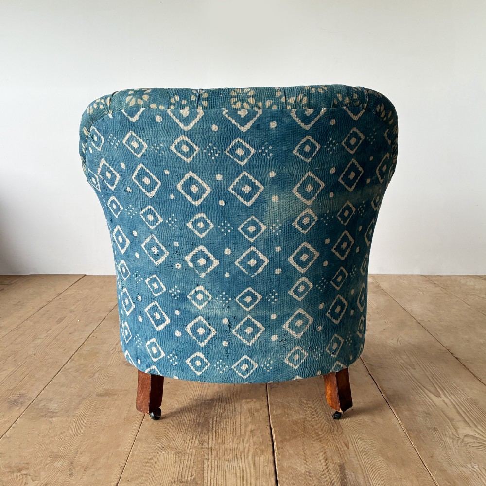 A 19th-century tub chair with blue and cream patterned fabric upholstery, button-tufted backrest, rolled arms, and tapered mahogany legs on brass castors. View V