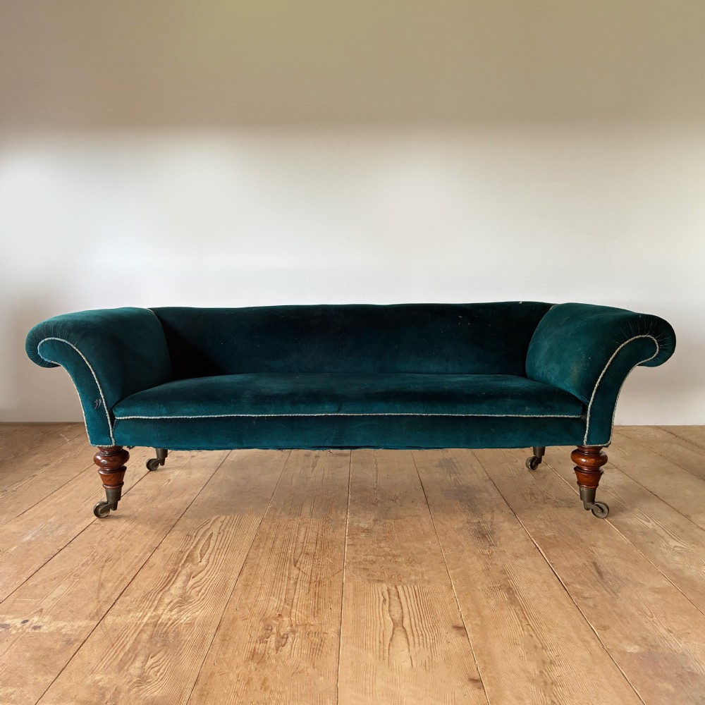 A 19th-century country house sofa upholstered in teal green velvet with scrolled arms, turned wooden legs, and brass castors.