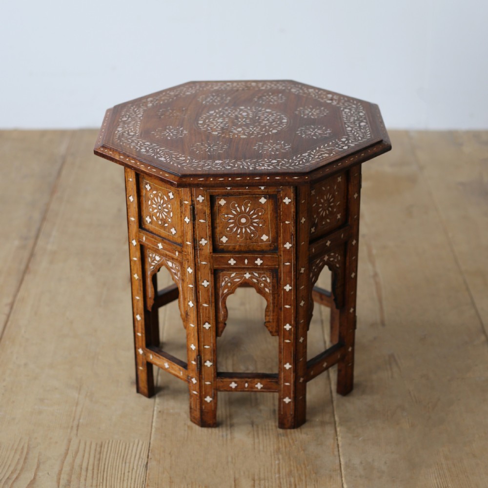 A 19th-century octagonal wooden side table with detailed white bone inlay forming floral and geometric patterns across the top and arched legs.