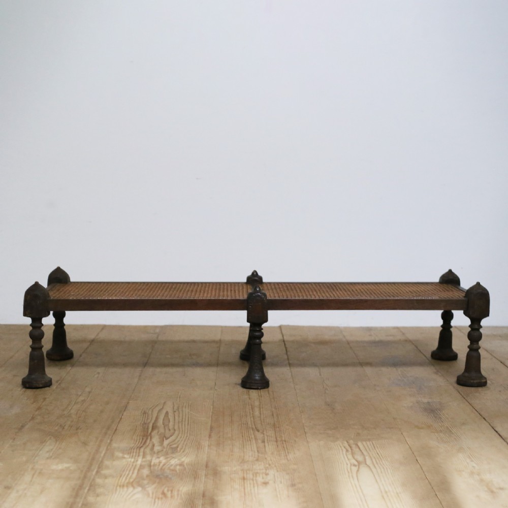 A low 19th-century Anglo-Indian daybed made from dark timber with turned legs, finial posts, and a woven cane top.