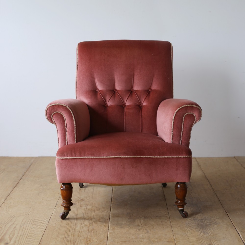 A 19th-century armchair upholstered in dusky rose pink velvet with a buttoned backrest, scroll arms, and turned wooden front legs set on castors.