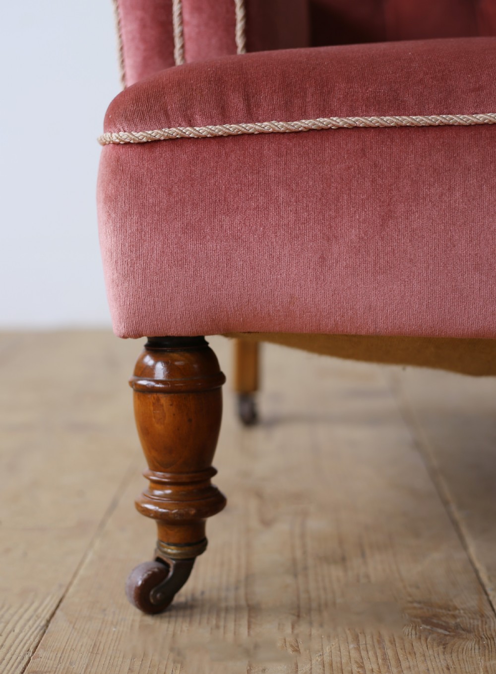 A 19th-century armchair upholstered in dusky rose pink velvet with a buttoned backrest, scroll arms, and turned wooden front legs set on castors. View III