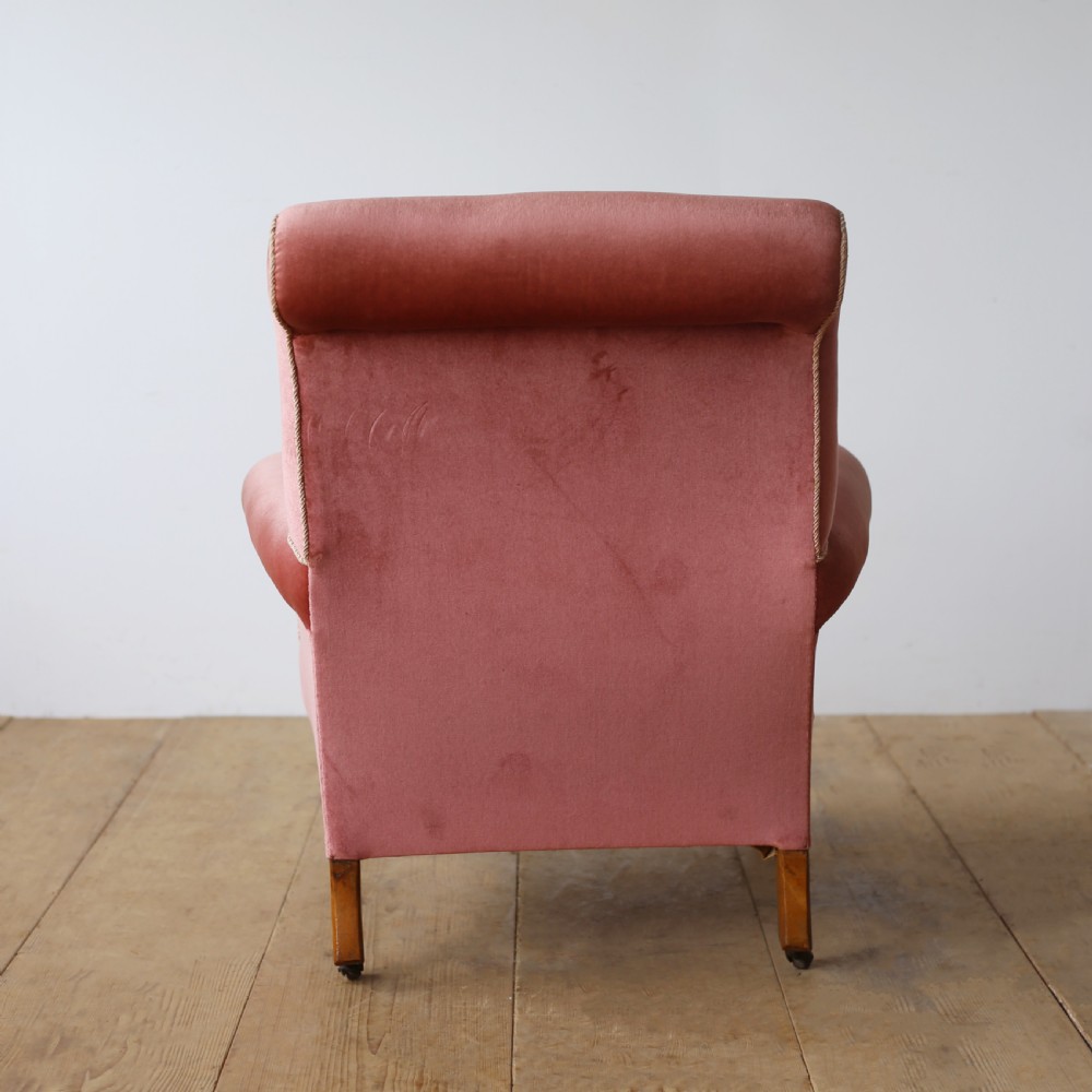 A 19th-century armchair upholstered in dusky rose pink velvet with a buttoned backrest, scroll arms, and turned wooden front legs set on castors. View V