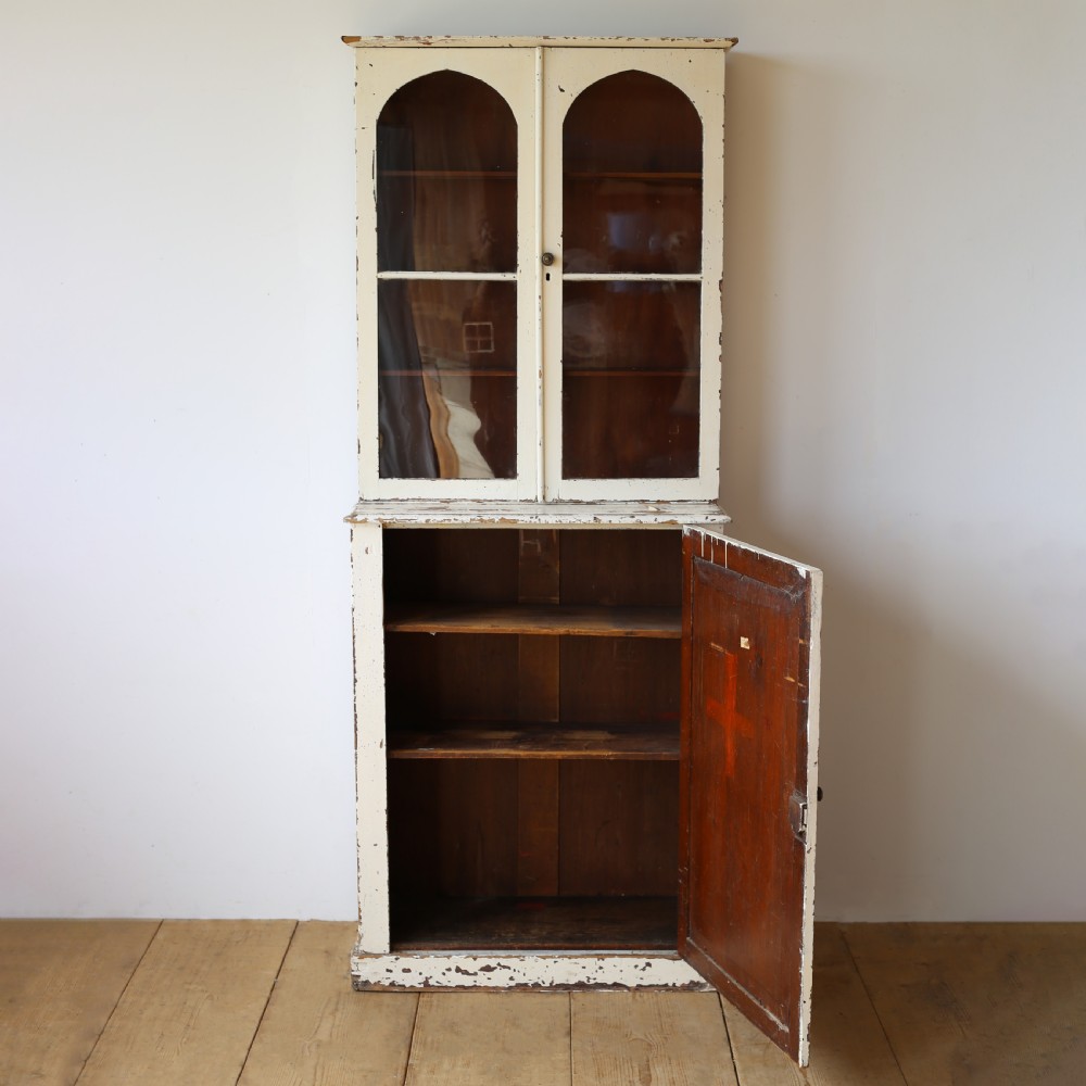 A tall 19th-century cream painted wooden cabinet featuring upper glazed doors with arched glass panels above a solid cupboard base. View II