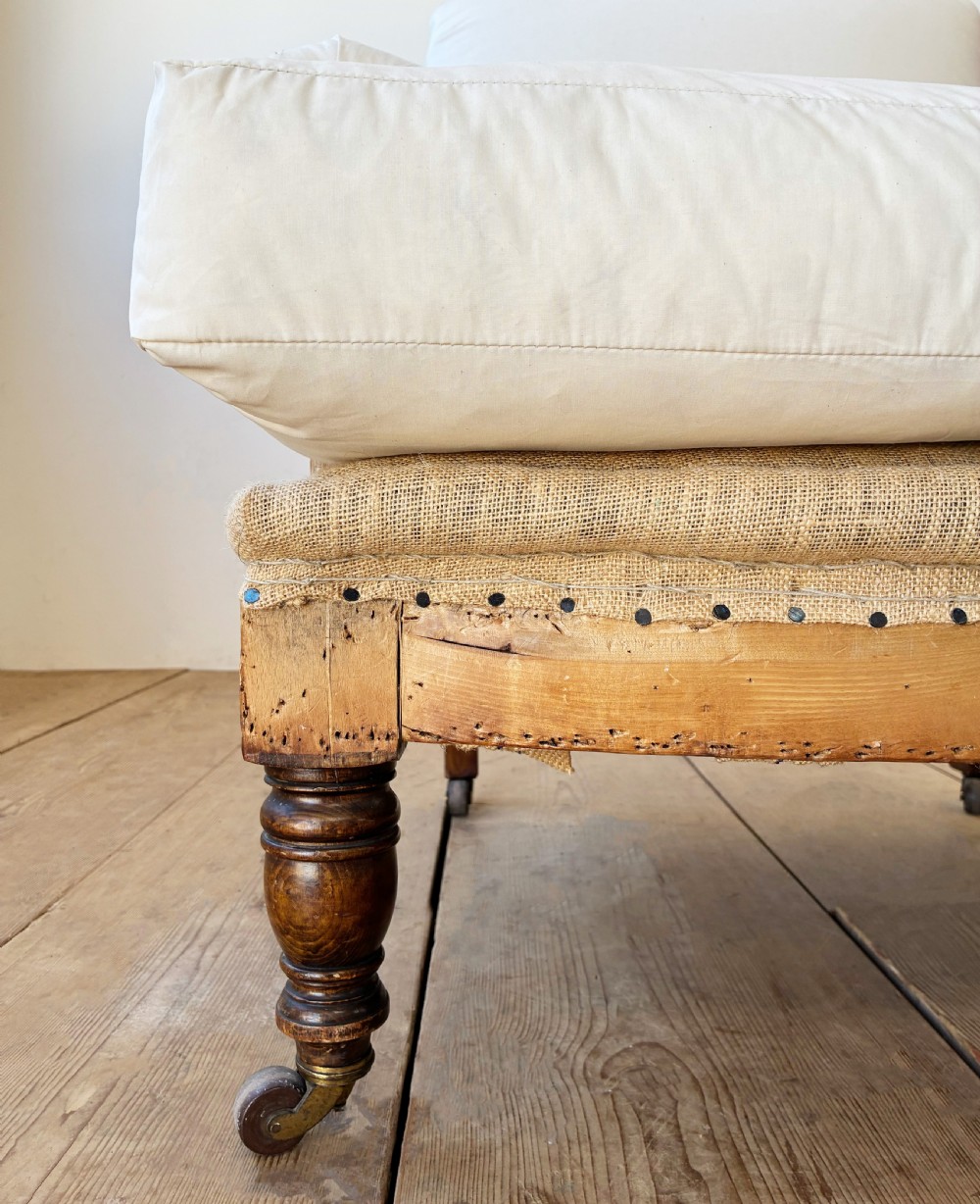 A nineteenth century Howard style armchair with cream calico fabric, deep seat cushion, scrolled arms, and turned timber legs on brass castors. View II