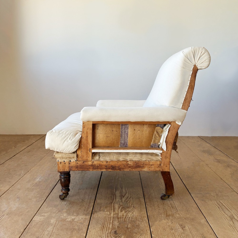 A nineteenth century Howard style armchair with cream calico fabric, deep seat cushion, scrolled arms, and turned timber legs on brass castors. View IV