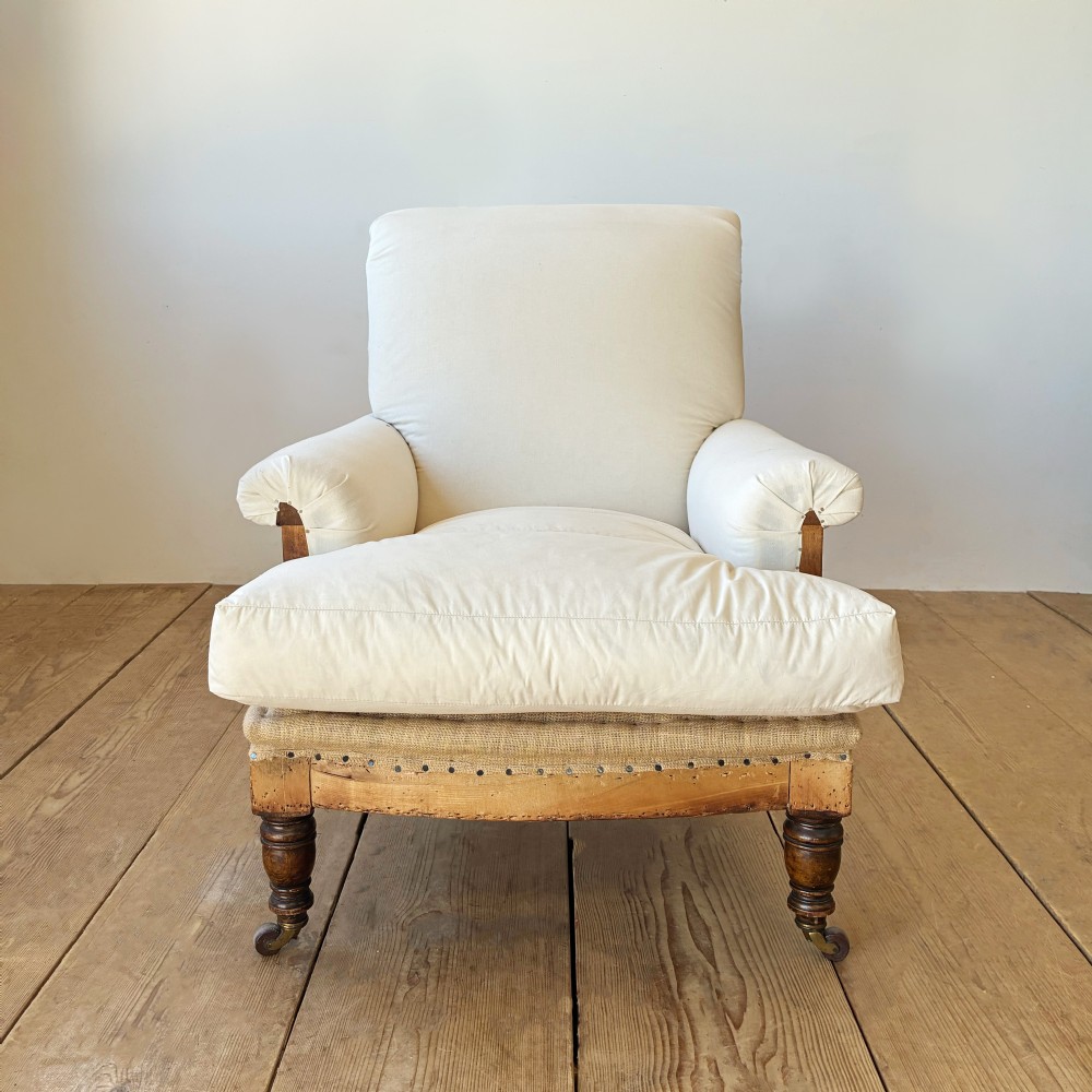 A nineteenth century Howard style armchair with cream calico fabric, deep seat cushion, scrolled arms, and turned timber legs on brass castors.