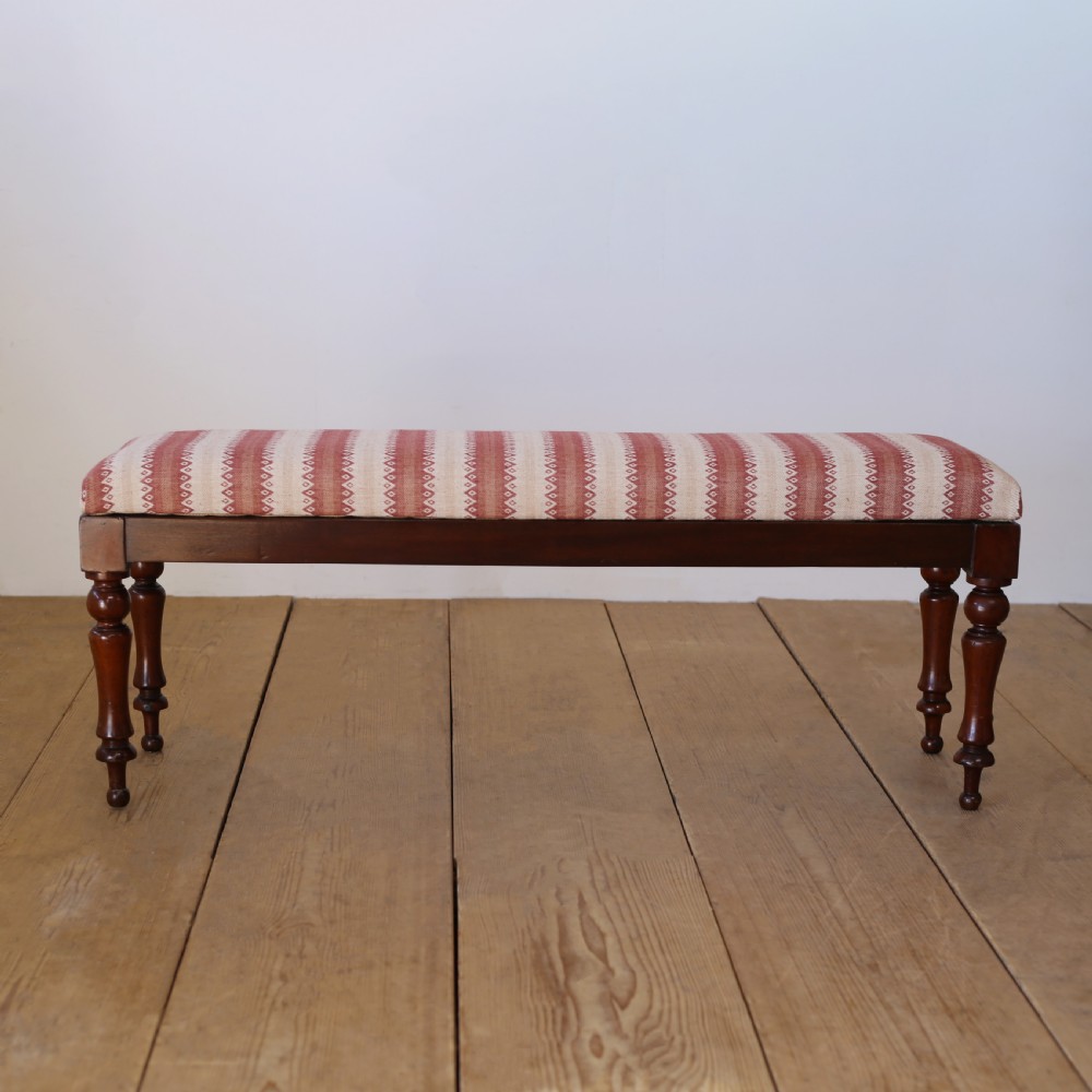 A long rectangular 19th-century window seat featuring a red and cream striped upholstered cushion set upon four turned dark hardwood legs.