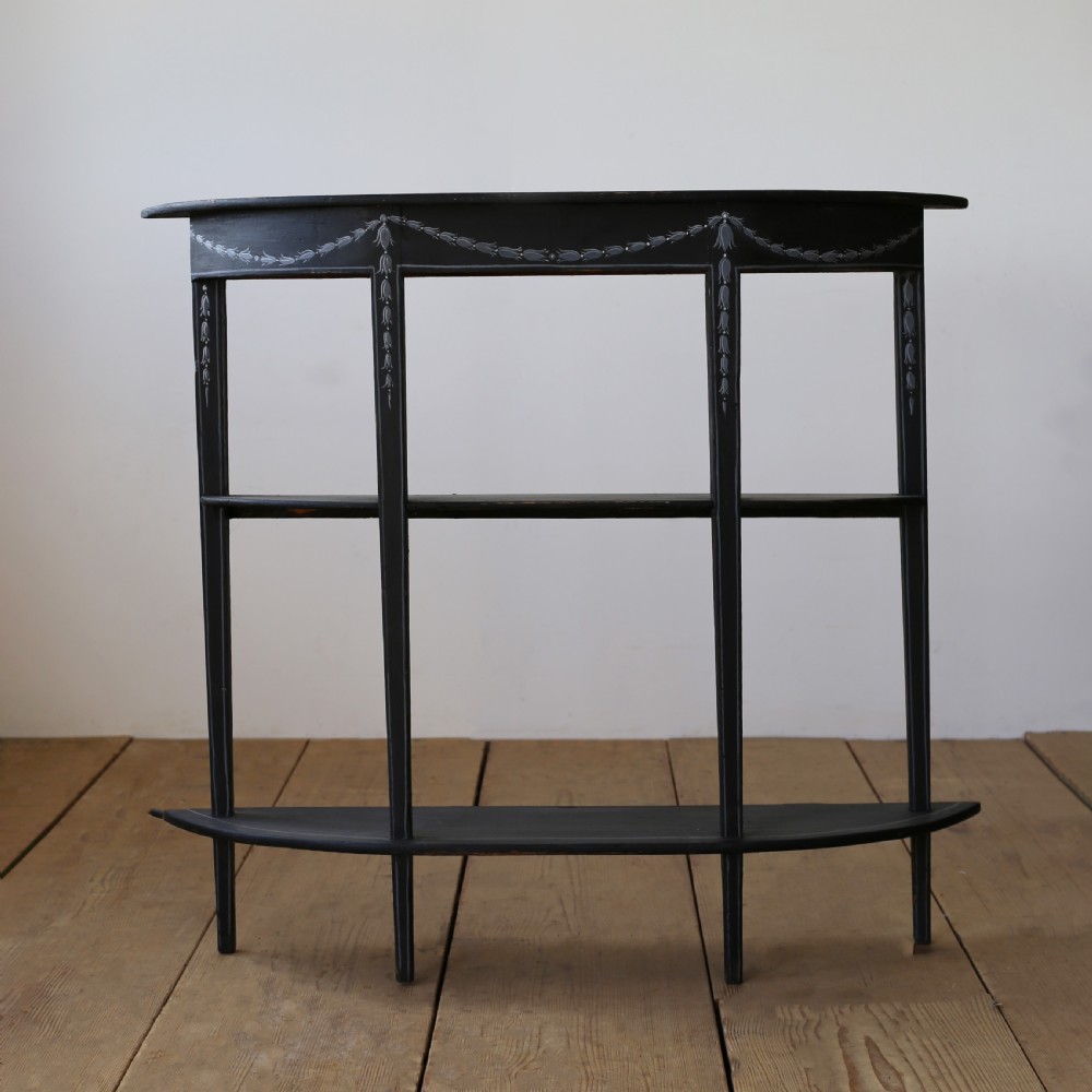 A black painted 19th-century demi-lune console table featuring painted floral swags on the apron and two open lower tiers.