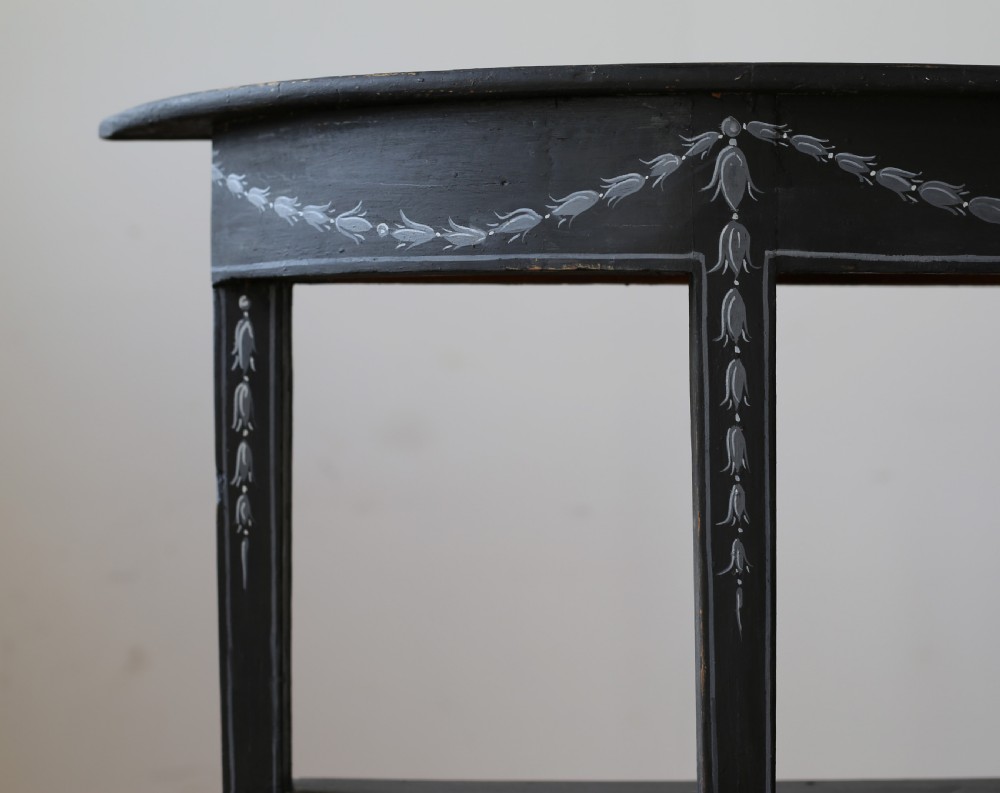 A black painted 19th-century demi-lune console table featuring painted floral swags on the apron and two open lower tiers. View II