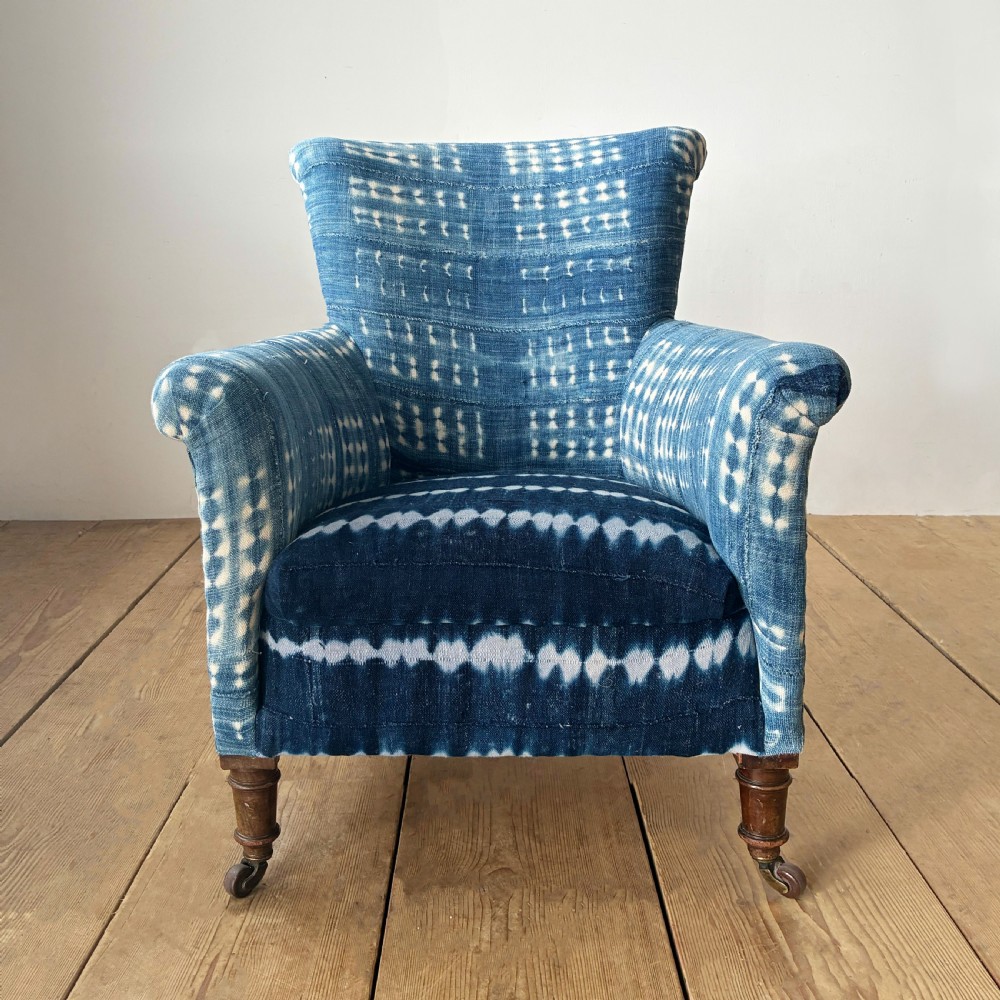 A 19th-century Woodstock armchair upholstered in indigo blue pattern-dyed cotton fabric, featuring scroll arms and turned wood legs on castors.