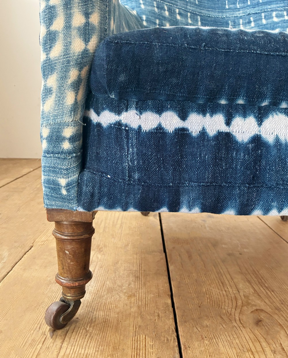 A 19th-century Woodstock armchair upholstered in indigo blue pattern-dyed cotton fabric, featuring scroll arms and turned wood legs on castors. View II