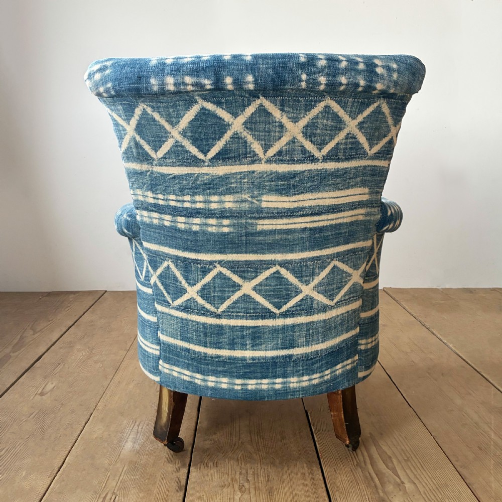 A 19th-century Woodstock armchair upholstered in indigo blue pattern-dyed cotton fabric, featuring scroll arms and turned wood legs on castors. View V