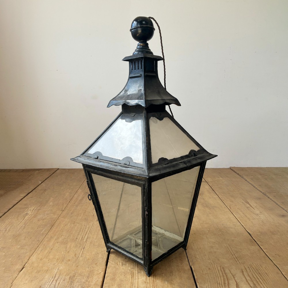 A black metal 19th-century lantern featuring clear glass panes, a tapered body, and a tiered pagoda-style canopy topped with a round finial.