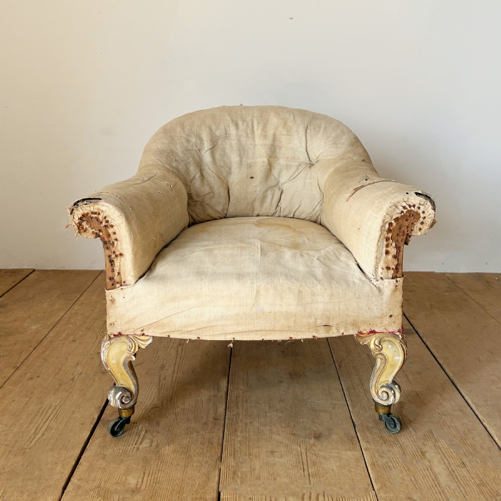 A 19th-century tub chair upholstered in natural calico fabric with carved giltwood cabriole front legs on metal castors.