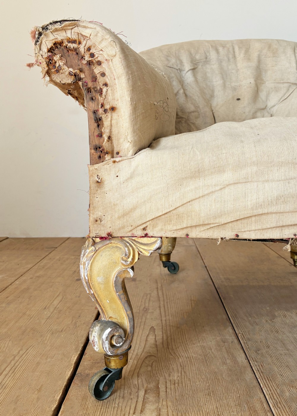 A 19th-century tub chair upholstered in natural calico fabric with carved giltwood cabriole front legs on metal castors. View II