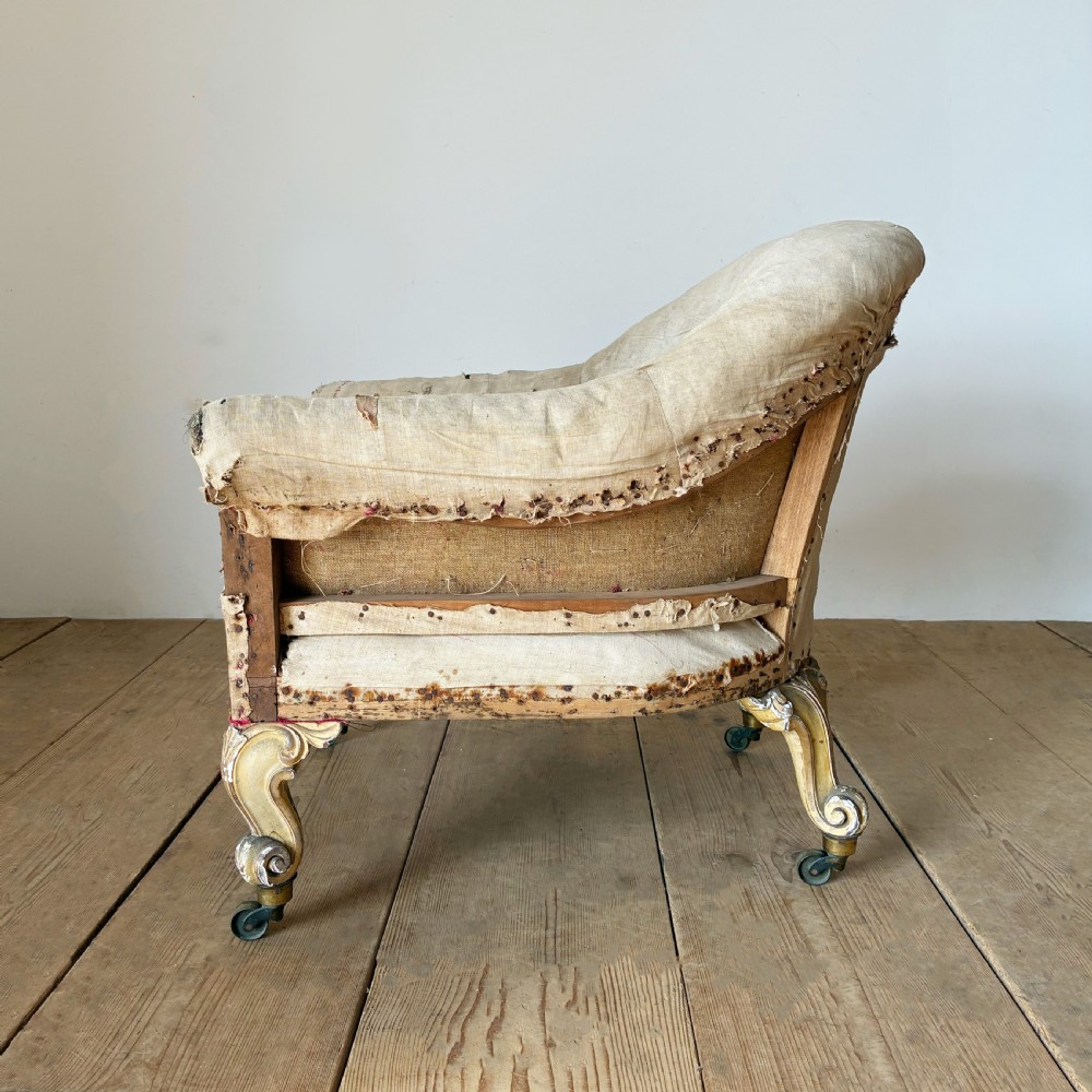 A 19th-century tub chair upholstered in natural calico fabric with carved giltwood cabriole front legs on metal castors. View IV