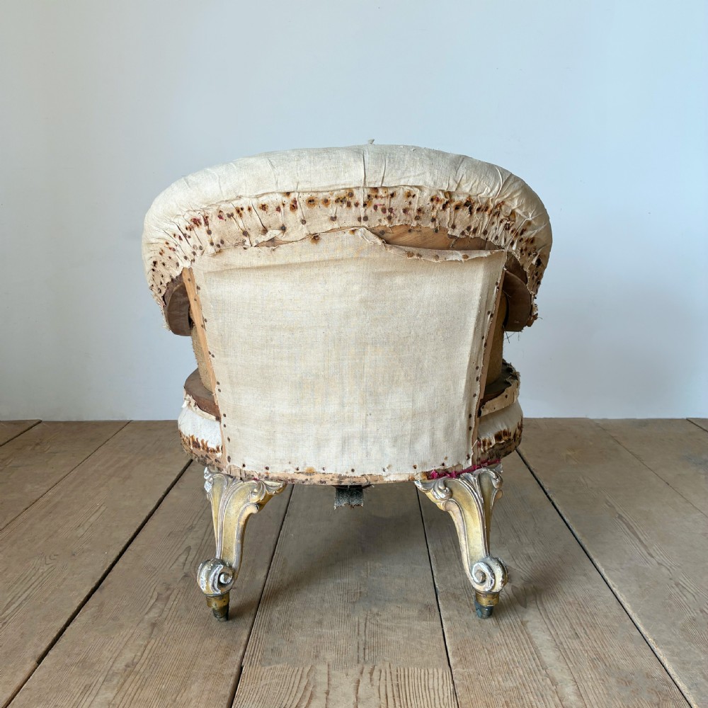 A 19th-century tub chair upholstered in natural calico fabric with carved giltwood cabriole front legs on metal castors. View V