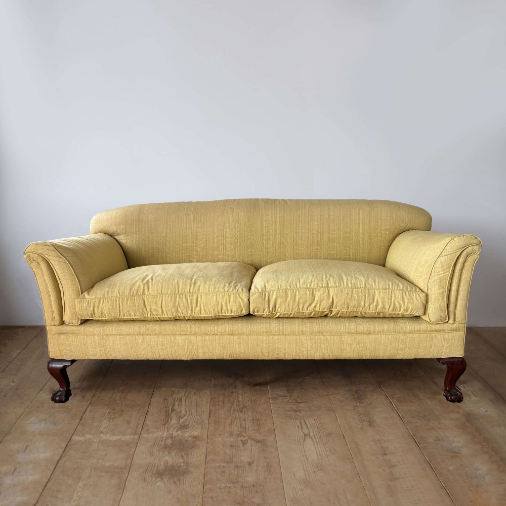 An upholstered two-seater sofa in yellow fabric featuring low scrolled arms, deep seat cushions, and carved dark mahogany cabriole legs with claw and ball feet.