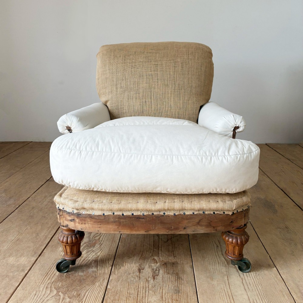 A nineteenth-century armchair frame in calico and hessian under-upholstery, featuring carved turned wooden front legs with metal castors.