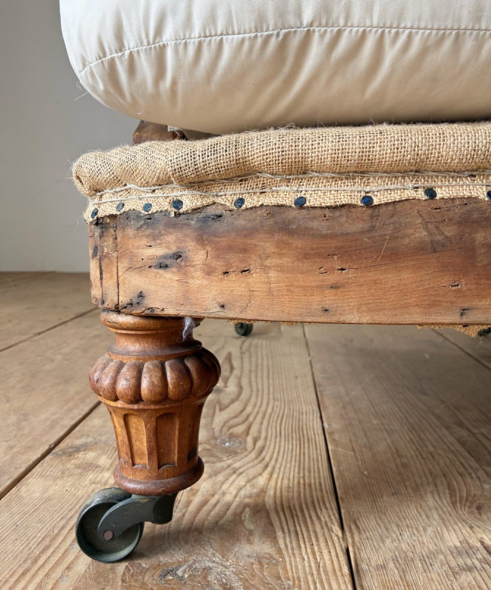 A nineteenth-century armchair frame in calico and hessian under-upholstery, featuring carved turned wooden front legs with metal castors. View II