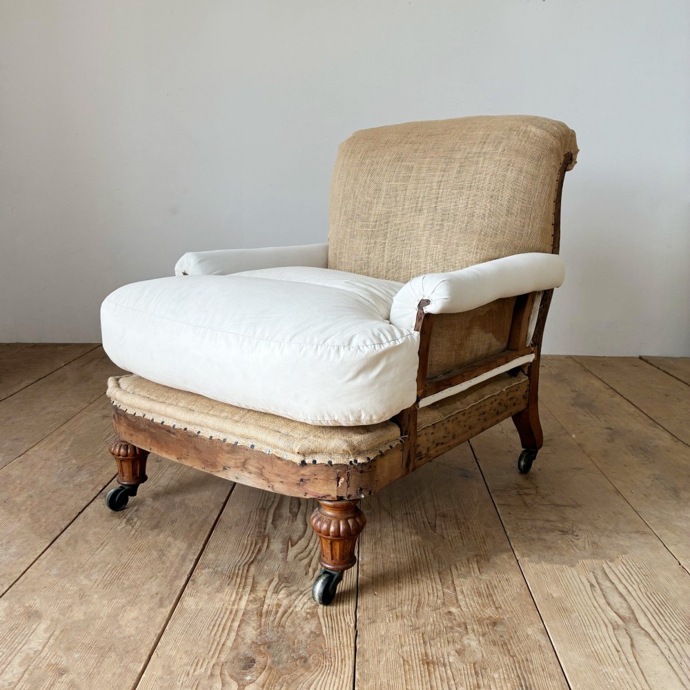 A nineteenth-century armchair frame in calico and hessian under-upholstery, featuring carved turned wooden front legs with metal castors. View III