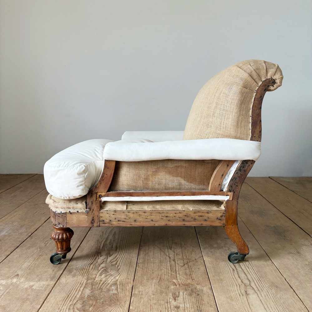 A nineteenth-century armchair frame in calico and hessian under-upholstery, featuring carved turned wooden front legs with metal castors. View IV