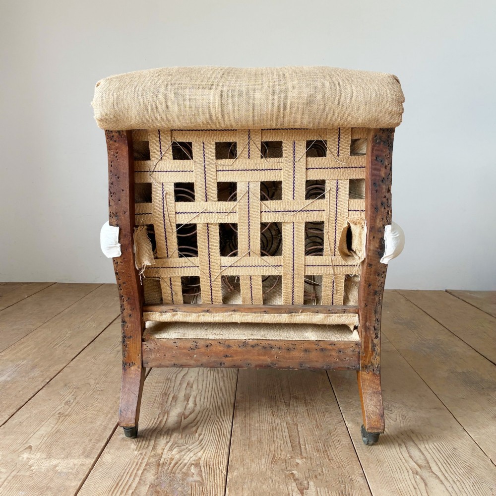 A nineteenth-century armchair frame in calico and hessian under-upholstery, featuring carved turned wooden front legs with metal castors. View V