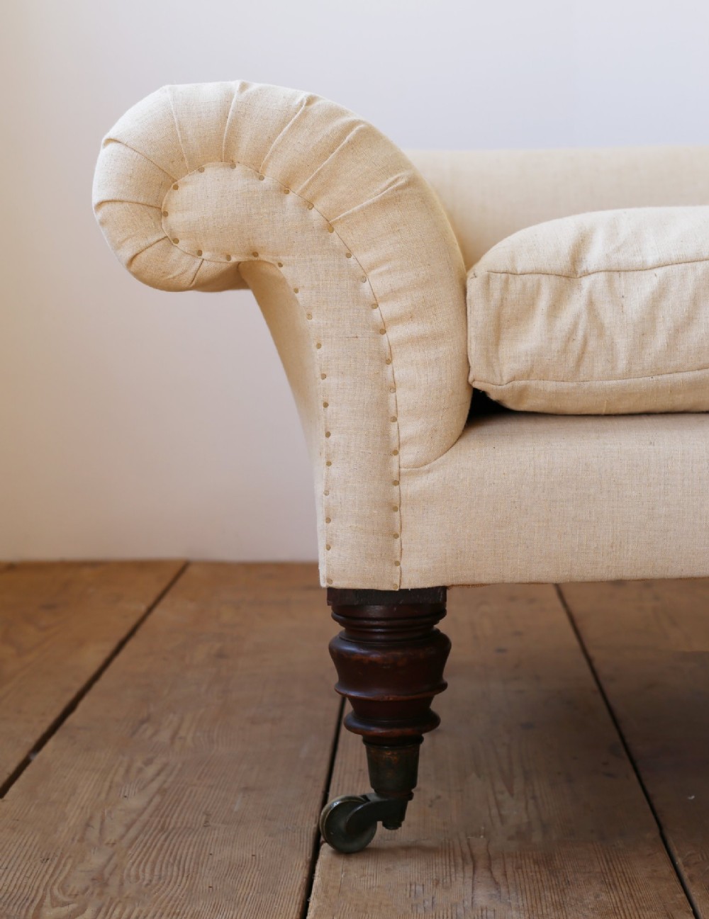A 19th-century English country house sofa upholstered in cream linen fabric, featuring scrolled arms, two loose seat cushions, and turned mahogany legs with brass castors. View II