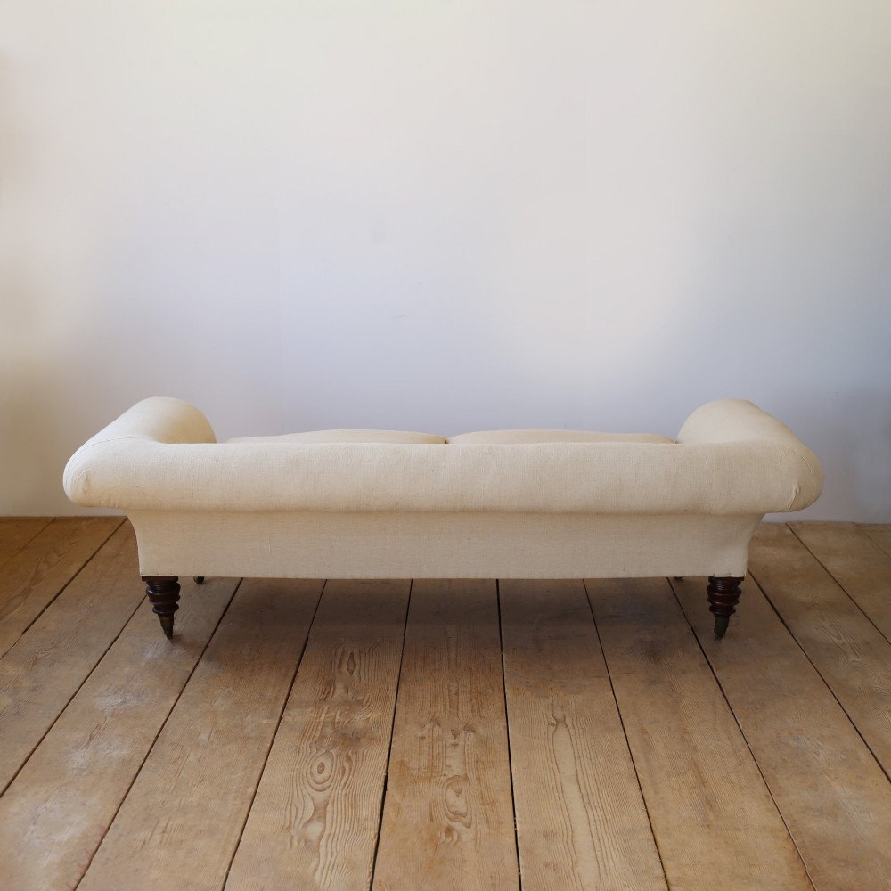 A 19th-century English country house sofa upholstered in cream linen fabric, featuring scrolled arms, two loose seat cushions, and turned mahogany legs with brass castors. View III