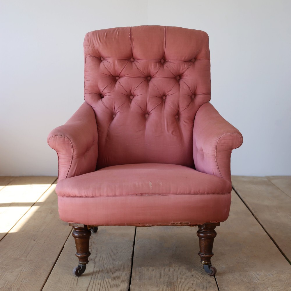 A 19th-century Victorian armchair upholstered in dusty rose fabric featuring a deep button back, padded armrests, and turned legs on brass castors.