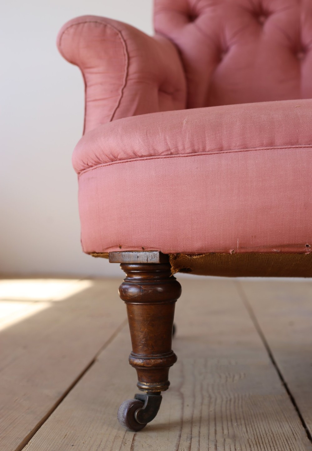 A 19th-century Victorian armchair upholstered in dusty rose fabric featuring a deep button back, padded armrests, and turned legs on brass castors. View II
