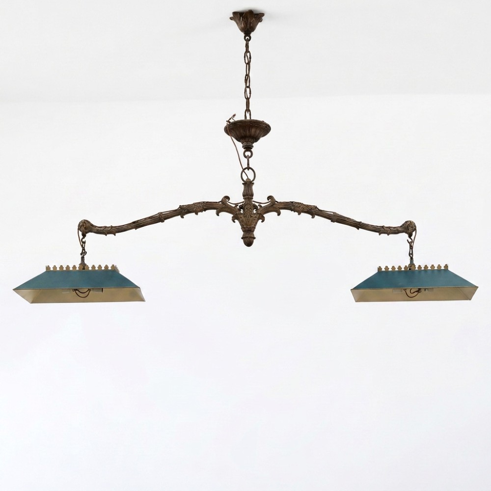 A 19th-century antique cast brass twin-shade billiard light fixture featuring scrollwork detailing and teal green trapezoidal shades.