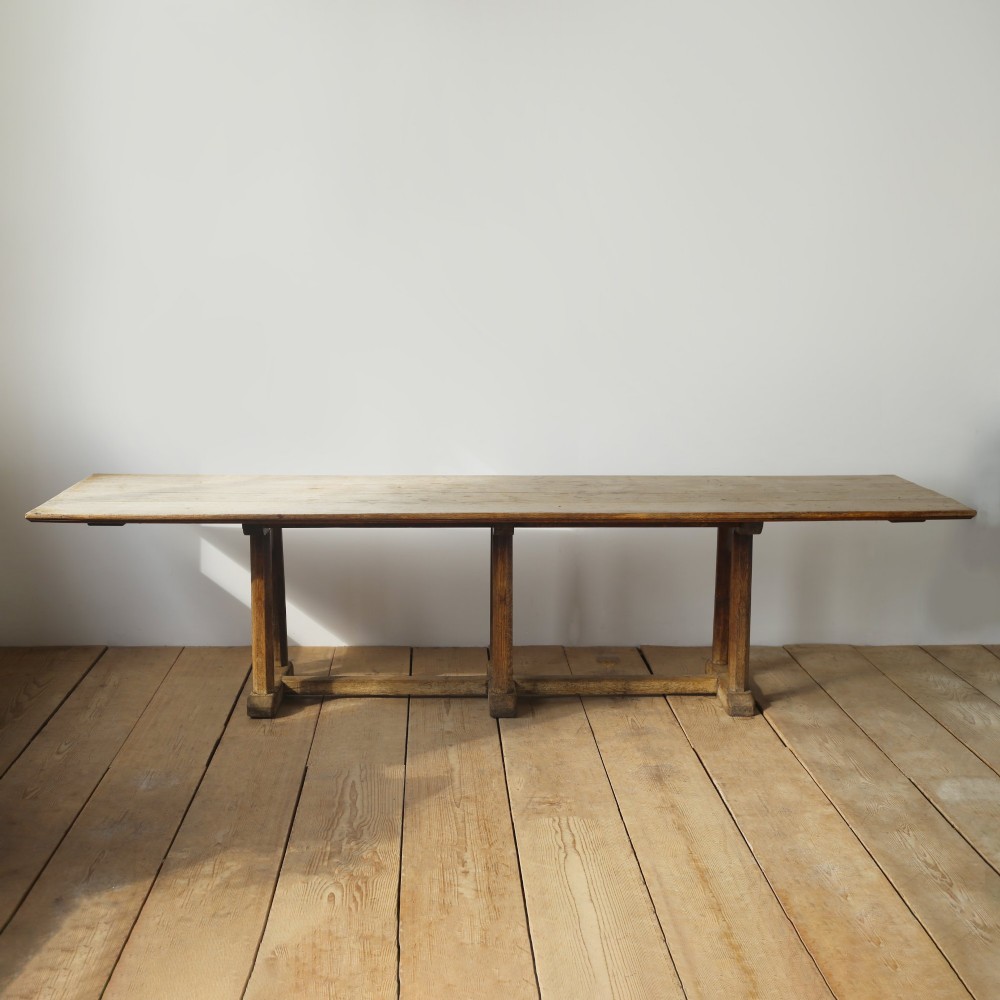 A long solid oak refectory table with a plank top and three sets of square legs connected by a low stretcher rail.