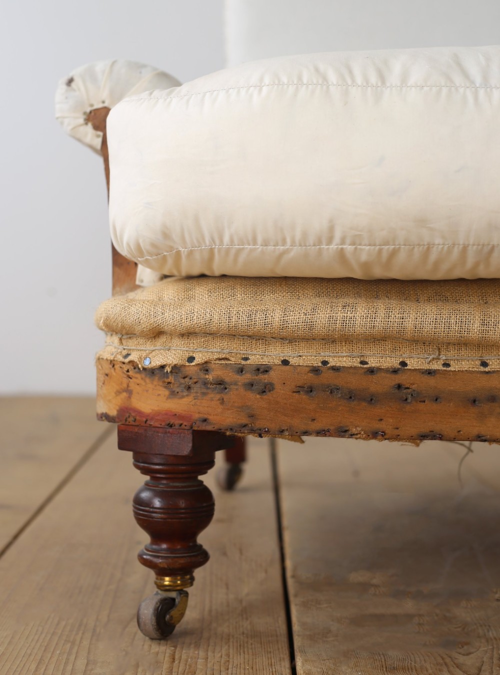 A 19th-century armchair upholstered in off-white calico featuring a thick seat cushion, scrolled armrests, and turned mahogany legs with brass castors. View II