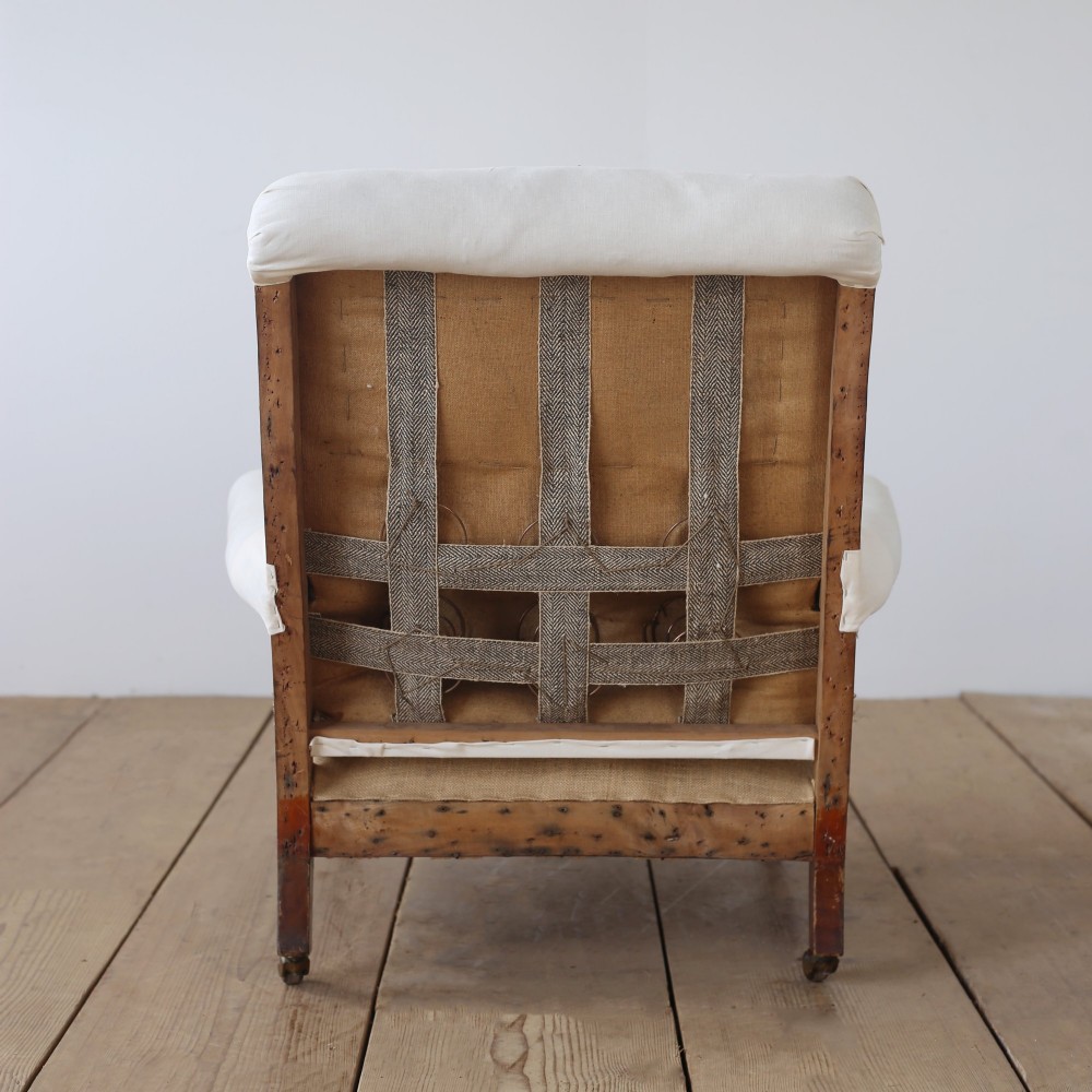A 19th-century armchair upholstered in off-white calico featuring a thick seat cushion, scrolled armrests, and turned mahogany legs with brass castors. View V