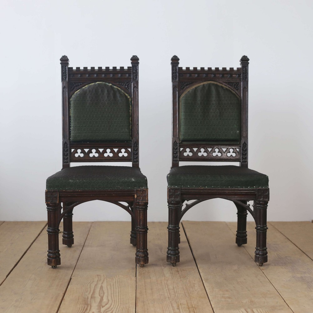 A pair of 19th-century Gothic Revival side chairs crafted from dark carved wood with dark green upholstered seats and backrests featuring pointed arch motifs.