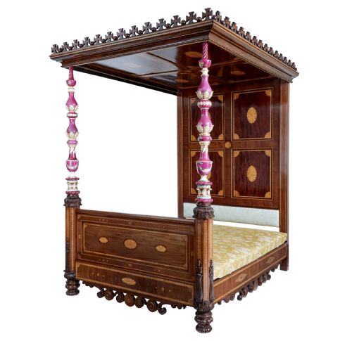 fig 3. A nineteenth-century mahogany four-poster bed frame featuring carved posts with pink porcelain sections, marquetry panelling, and an ornate trefoil canopy trim.
