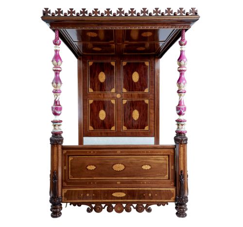 fig 4. A nineteenth-century mahogany four-poster bed frame featuring carved posts with pink porcelain sections, marquetry panelling, and an ornate trefoil canopy trim.