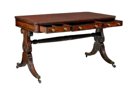 fig 1. A 19th-century William IV mahogany library desk featuring three frieze drawers with brass knobs, carved scroll end supports, and a turned stretcher on brass castors.