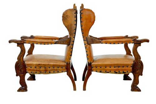 fig 1. A pair of 19th-century oak armchairs featuring tan leather upholstery with central embossed medallions, brass stud trim, and carved supports.