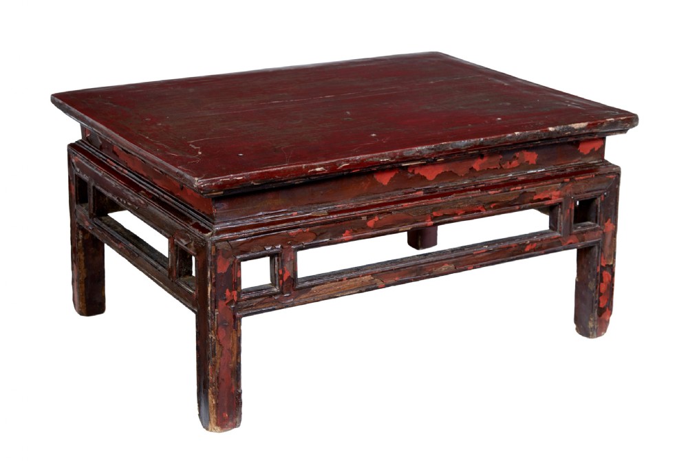 An 18th-century Chinese low table featuring a distressed red lacquer finish, straight square legs, and geometric openwork aprons.