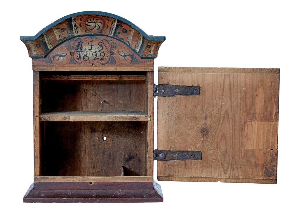 An early 19th-century Swedish painted wall cupboard featuring an arched crest, dark teal trim, and painted floral motifs in terracotta and ochre with the date 1822. View II